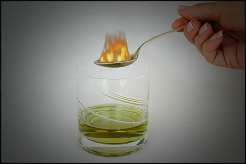 A spoon above the absinthe drink in a glass, with sugar on fire.